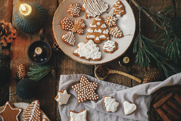 Χριστουγεννιάτικα μπισκότα σε ρουστίκ τραπέζι με χαρτοπετσέτα, κερί, διακοσμήσεις, μπαχαρικά. Επίπεδη. Ατμοσφαιρική κυκλοθυμική εικόνα. Φτιάχνω κομψά χριστουγεννιάτικα μπισκότα με μελόψωμο. Καλές γιορτές.! - Φωτογραφία, εικόνα