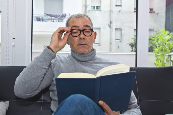 mature man reading on the sofa at home - Foto, afbeelding