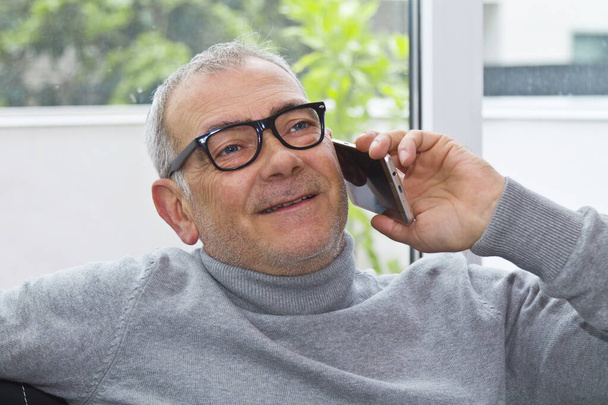 mature man using the phone on the sofa at home - Foto, Bild