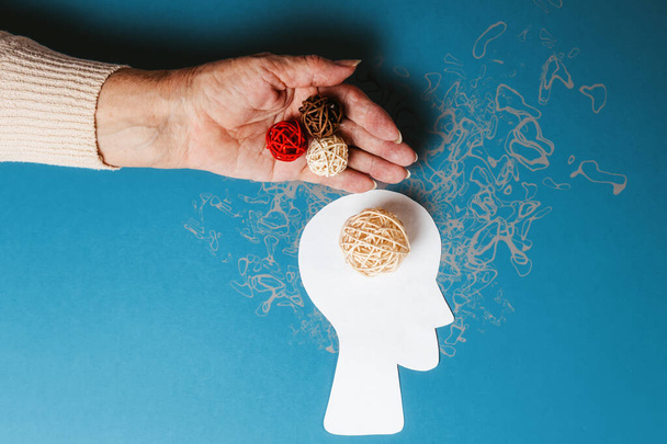 World Alzheimer's Day. On the palm of an old woman there are three woven multicolored balls, and a white ball on a paper silhouette of a head. The concept of mental problems. - Fotoğraf, Görsel