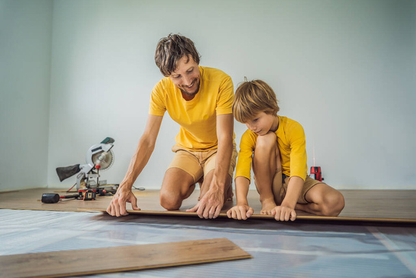 Father and son installing new wooden laminate flooring on a warm film floor. Infrared floor heating system under laminate floor - Foto, immagini