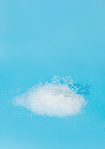 Um floco de neve de cristal em uma pilha de neve em um fundo azul. Conceito mínimo de inverno. - Foto, Imagem