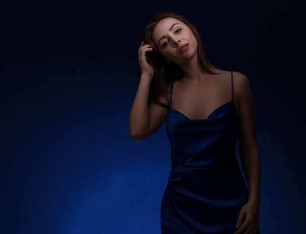 Mujer morena joven y linda en vestido blu posando sobre fondo azul oscuro espacio libre para el texto - Foto, Imagen