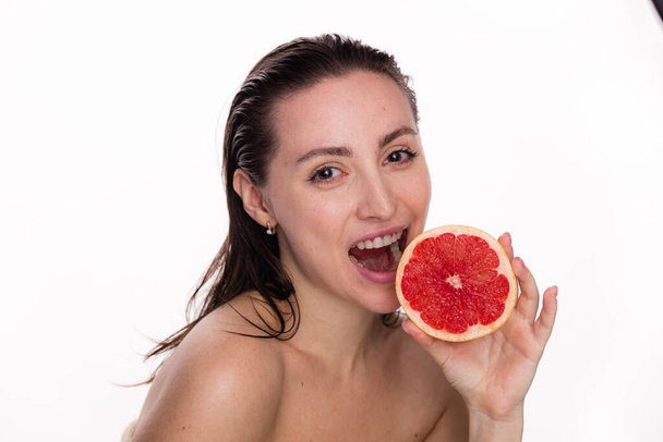 Boldog fiatal gyönyörű nő egészséges ragyogás tökéletes sima és nedves bőr tartja darab piros grapefruit közel arc. Természetes kozmetikumok, bőrápolás, wellness, arckezelés, kozmetológia, diéta koncepció. - Fotó, kép
