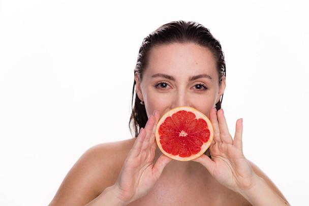 Happy young beautiful woman with healthy glow perfect smooth and wet skin holds piece of red grapefruit near face. Natural cosmetics, skincare, wellness, facial treatment, cosmetology, diet concept. - Photo, Image