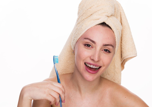 Słodka i podekscytowana piękna kobieta trzyma szczoteczkę do zębów i nosi ręcznik na głowie. Kobieta ma czystą skórę pokazuje białe zęby, pozuje z nagim ciałem izolowane na białym tle - Zdjęcie, obraz
