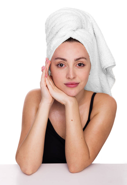 Portrét mladé šťastné ženy po sprše s ručníkem na hlavě, opírající se o stůl nebo prázdnou bílou plakátovou kartu na bílém. Koncepce zdravotní péče, krásy a mládeže - Fotografie, Obrázek