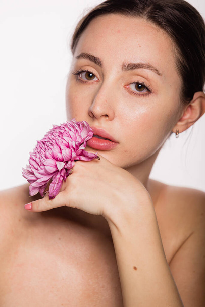 Ładna kobieta z kwiatem w ręku przy twarzy nagie ramiona czysta skóra. Koncepcja pielęgnacji skóry i Spa na białym tle. Kobieta patrząca w kamerę - Zdjęcie, obraz