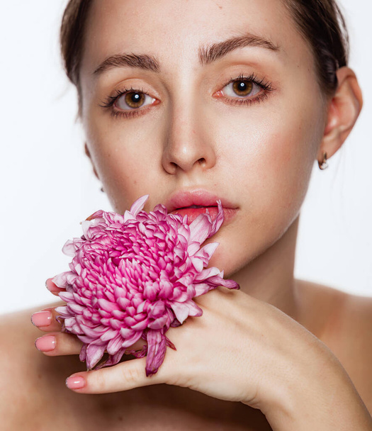 Pretty woman with flower in her hands near the face naked shoulders clear skin. Skin care and Spa concept on white background. Woman looking at camera - Fotoğraf, Görsel