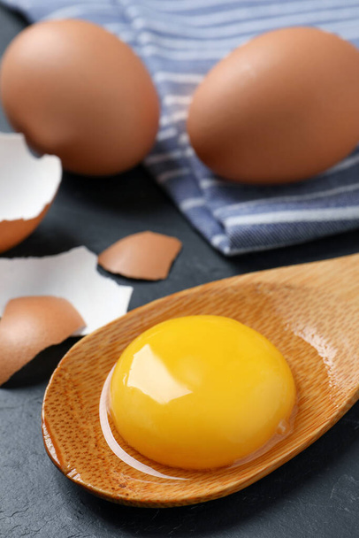 Wooden spoon with raw egg yolk on black table, closeup - Photo, Image