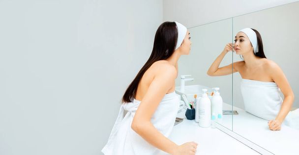 Portrait of a young beautiful woman looking at her face in the mirror. Web banner. Copy space. The concept of professional skin care. - Photo, Image