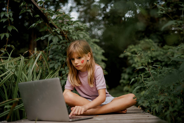 Cute child is playing on laptop in the garden - Zdjęcie, obraz