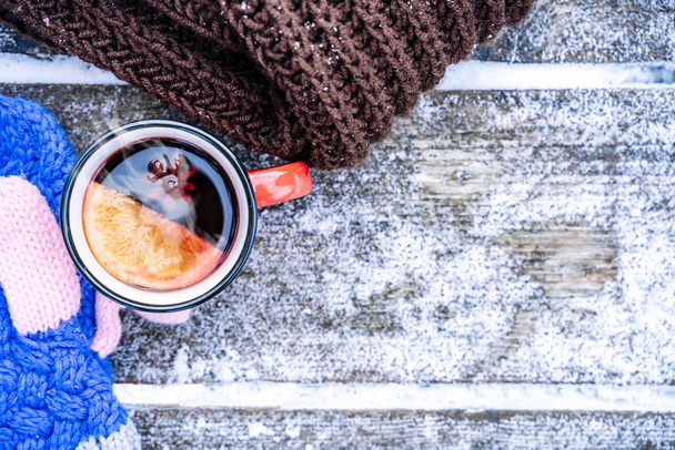Вино или чай на деревянном фоне во время снегопада в лесу. Зимние горячие напитки с ароматическими специями корицы, кардамона и апельсина. Тепло, комфорт и атмосфера декабрьской природы - Фото, изображение
