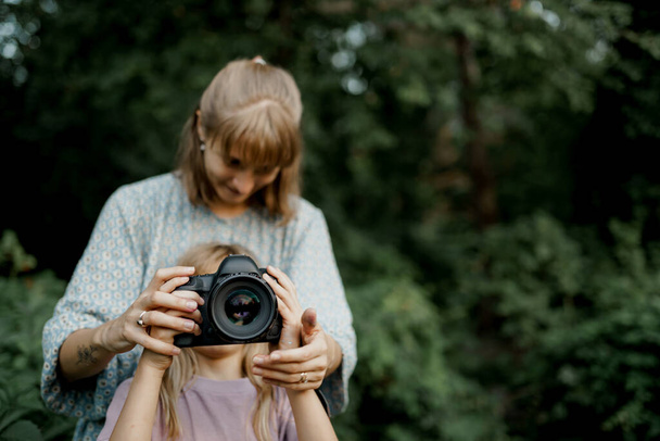 Mother is teaching her young daughter to use a camera outside in spring nature - Foto, Imagen