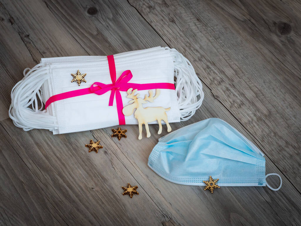 Maschere igieniche bianche e blu come regalo legato con nastro viola e renne in legno e sfondo decorazione fiocco di neve, isolamento vacanze di Natale e concetto pandemia coronavirus - Foto, immagini