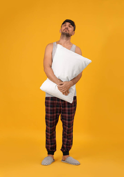 Man with pillow and eye mask in sleepwalking state on yellow background - 写真・画像