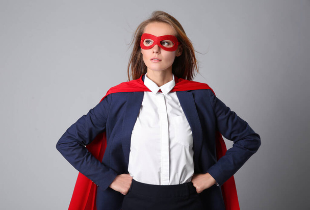 Confident businesswoman wearing superhero cape and mask on light grey background - Valokuva, kuva