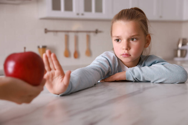 Cute little girl refusing to eat apple in kitchen, closeup - Φωτογραφία, εικόνα