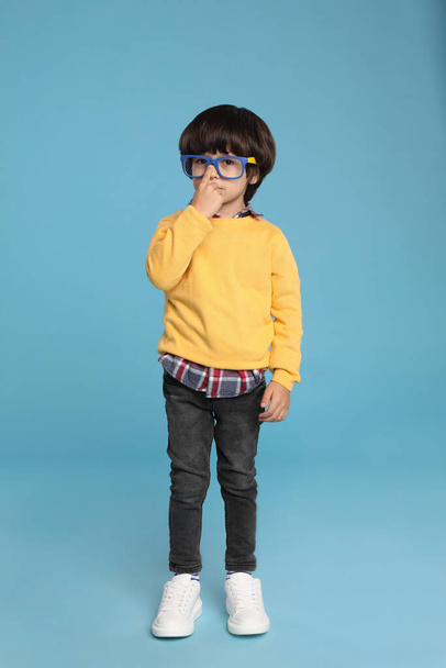 Cute little boy with funny glasses on light blue background - Фото, изображение