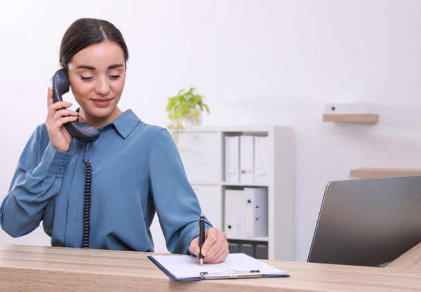Female receptionist with clipboard talking on phone at workplace - Foto, Imagen