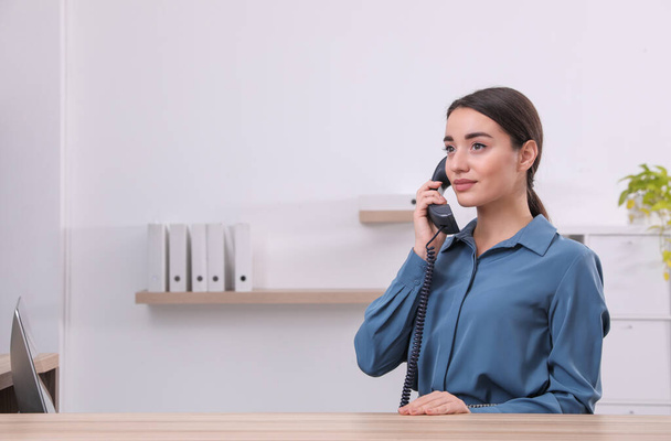 Female receptionist talking on phone at workplace. Space for text - Foto, Bild