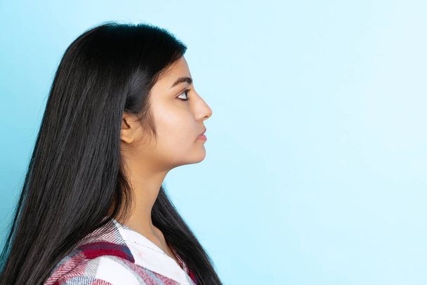 Profile view of young girl, student with long black glossy hair isolated on light blue studio backgroud - 写真・画像
