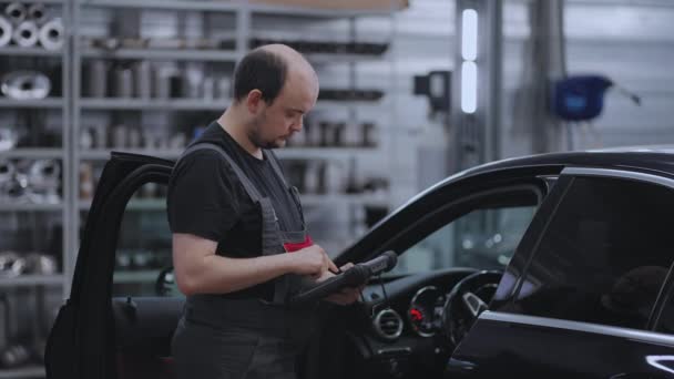 Diagnóstico de coches. Un mecánico en un servicio de primer plano sostiene una tableta en sus manos y presiona la pantalla cerca del coche - Metraje, vídeo