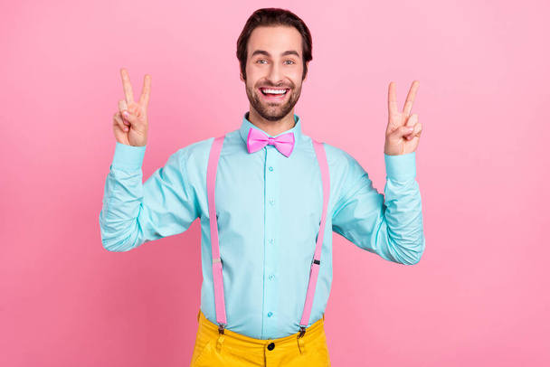 Photo of pretty impressed young man wear turquoise outfit smiling showing two v-signs isolated pink color background - Foto, immagini