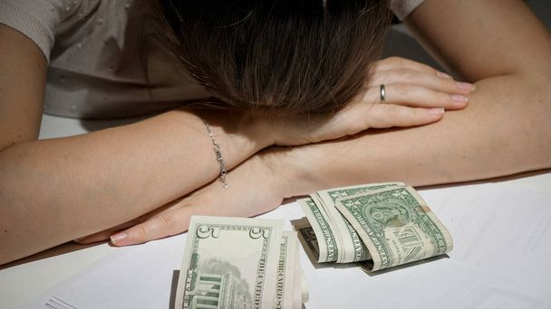 Наголошена жінка з великим боргом і фінансовими проблемами лежить на столі поруч з декількома грошовими купюрами
 - Фото, зображення