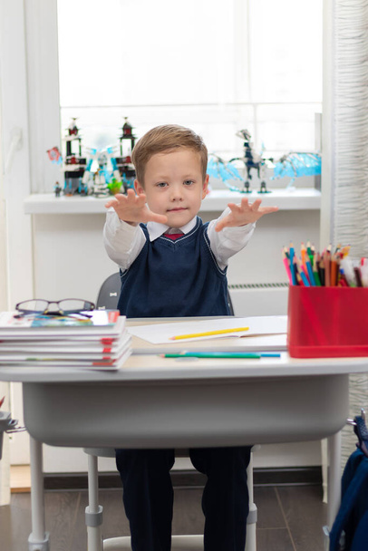 Niño lindo de primer grado en uniforme escolar en casa durante un descanso tonteando mientras está sentado en su escritorio. Enfoque selectivo. Primer plano. Retrato - Foto, imagen