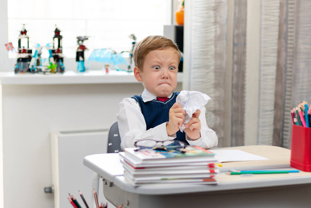 Niño lindo de primer grado en uniforme escolar en casa durante un descanso tonteando mientras está sentado en su escritorio. Enfoque selectivo. Primer plano. Retrato - Foto, imagen