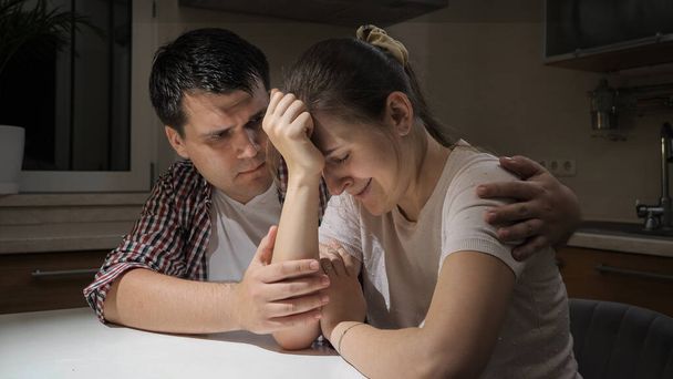 Yougn weinende Frau, die unter Depressionen und Problemen leidet, sitzt mit ihrem Mann in der Küche - Foto, Bild