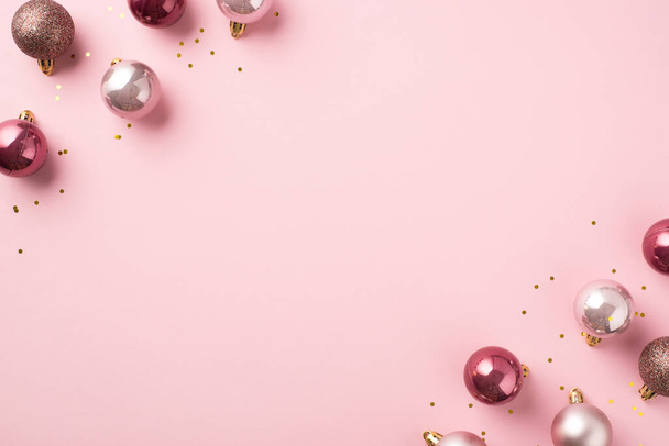 Top view photo of pink christmas tree decorations balls and gold sequins on isolated pastel pink background with copyspace - Photo, Image