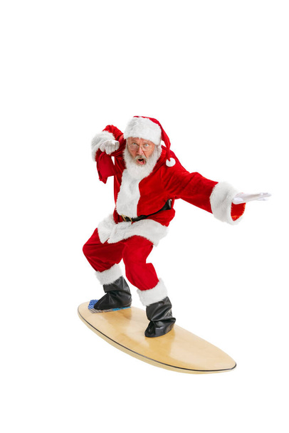 Portrait of emotional Santa Claus in red-white costume standing surfboard isolated on white background. Merry Christmas concept - Photo, image