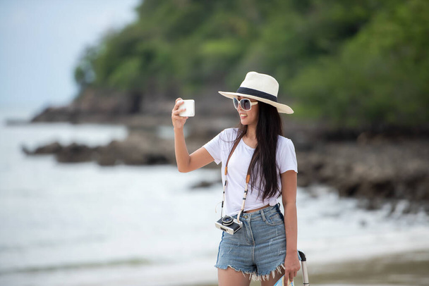 Happy traveler and tourism young women travel summer on the beach. Asian smiling people holding smartphone take photo  for relax outdoor destination leisure trip travel in holiday - 写真・画像
