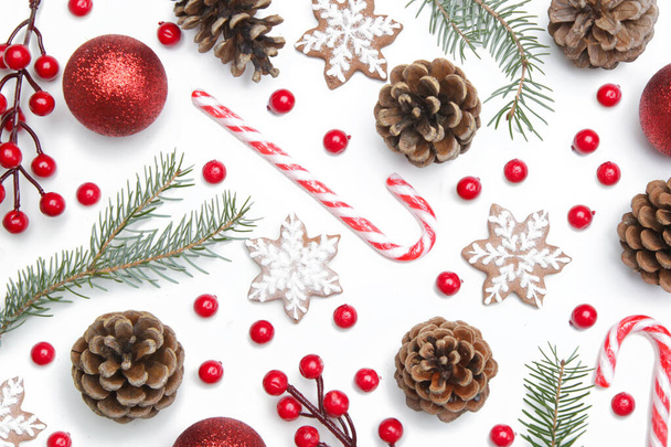 Ramas de árboles de Navidad, conos de coníferas y bayas rojas, galletas y adornos navideños, vista superior sobre fondo blanco. Navidad, vacaciones de invierno, concepto de año nuevo. - Foto, imagen