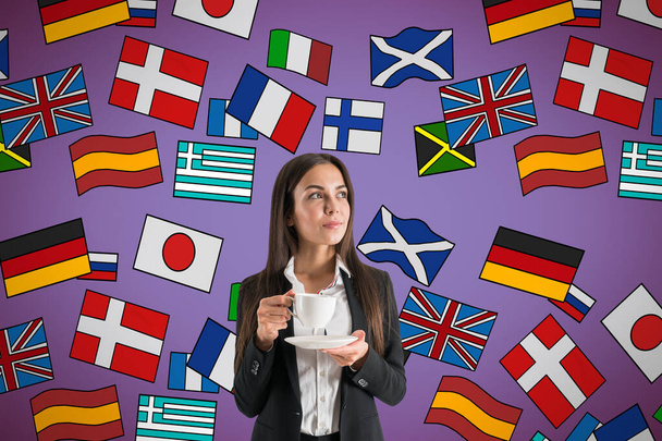 Portrait of attractive young european businesswoman drinking coffee with abstract colorful flag drawings. Travel, translation and language learning concept - Foto, imagen