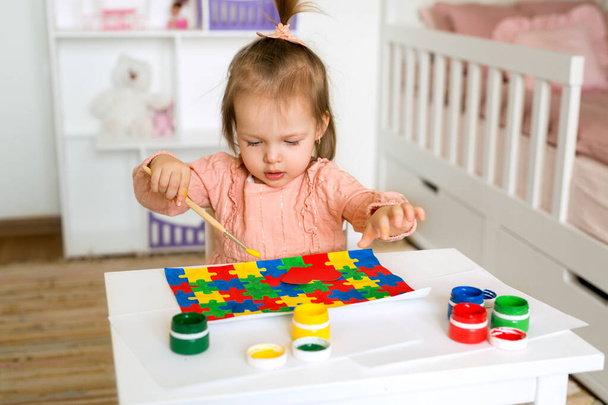 A one-year-old child draws with gouache paints, coloring a drawing with colorful puzzles. World Autism Awareness Day. A preschooler at the table in the nursery learns to draw with a brush - Photo, Image
