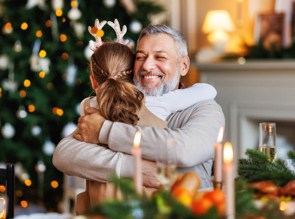 Kleine Enkelin umarmt glücklich lächelnden Opa beim Weihnachtsessen zu Hause - Foto, Bild