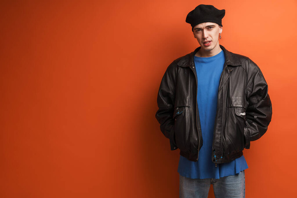 Young fashionable white man wearing leather jacket and beret standing posing over red background - Foto, Imagen