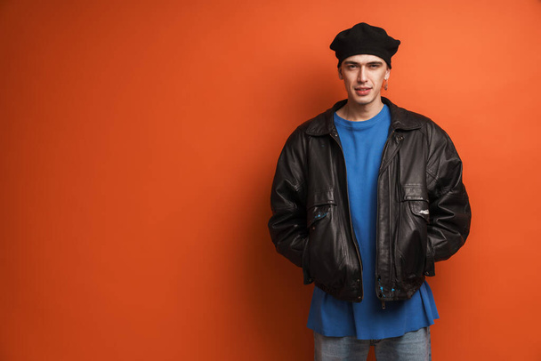 Young fashionable white man wearing leather jacket and beret standing posing over red background - Foto, imagen
