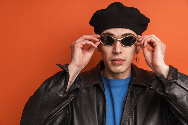Young fashionable white man wearing leather jacket and beret standing posing over red background - Fotó, kép