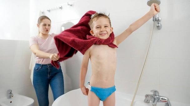 Tiro engraçado de menino sorridente feliz com a mãe jogando no banheiro e fingindo ser herói de quadrinhos - Foto, Imagem