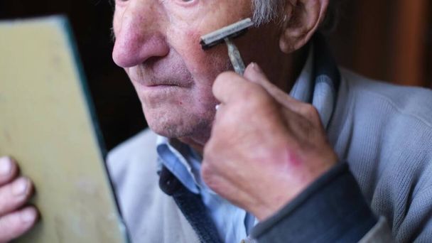 Ein älterer Mann rasiert sich vor einem Spiegel das Gesicht. Der Rentner rasiert sich den Bart ab. - Foto, Bild