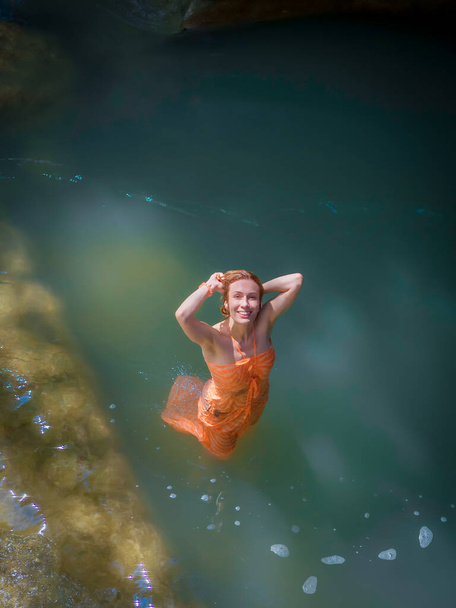 Dziewczyna w mokrej sukience uśmiechnięta spogląda w górę stojąc w wodzie w wąwozie kanionu oświetlonym słońcem - Zdjęcie, obraz