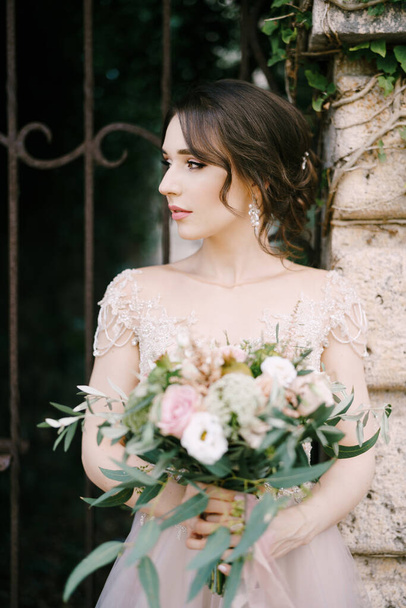 Menyasszony csokor virággal áll a kovácsolt kapunál. Portré - Fotó, kép