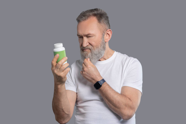 A bearded man holding a jar with vitamins - Фото, зображення