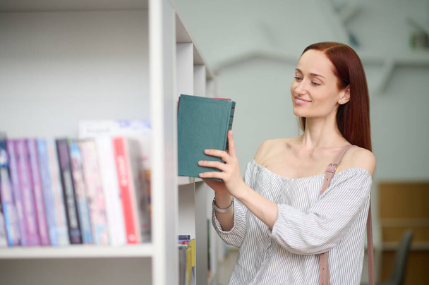 Woman putting book on shelf in library - Фото, изображение