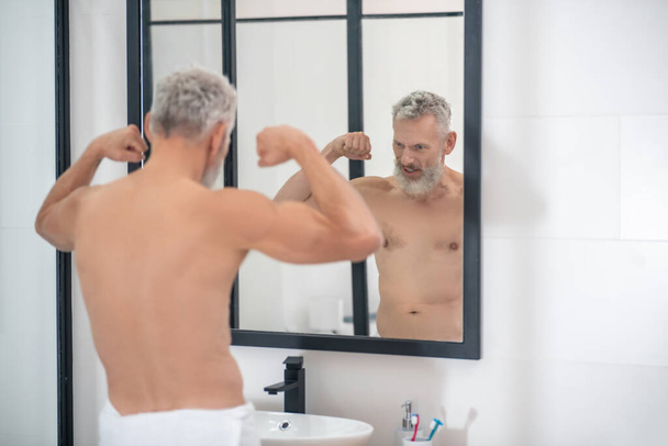Man straining muscles of arms looking in mirror - Fotografie, Obrázek