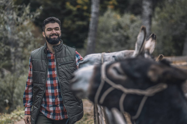 Bearded farmer standing near the donkey in a cattle-pen - Zdjęcie, obraz